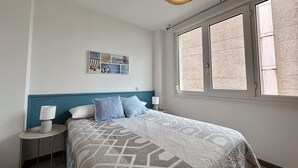 A bedroom with a bed, a nightstand, a wall-mounted lamp, a window, and a ceiling light fixture. - Benvenuti 30026 Apartment in Somo (Somo)