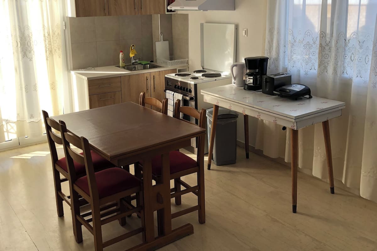 A compact kitchen with wooden cabinets, a dining table with chairs, a small stove, and a coffee maker.