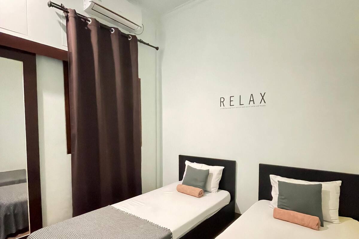 A hotel room with two single beds, a mirror, an air conditioning unit, and a wall with the word "RELAX" written on it.