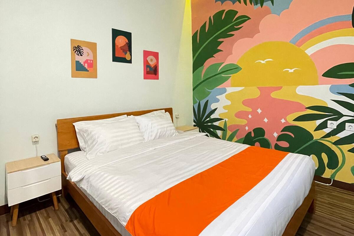 A bedroom with a wooden bed, white bedding, a nightstand, and a colorful mural on the wall.