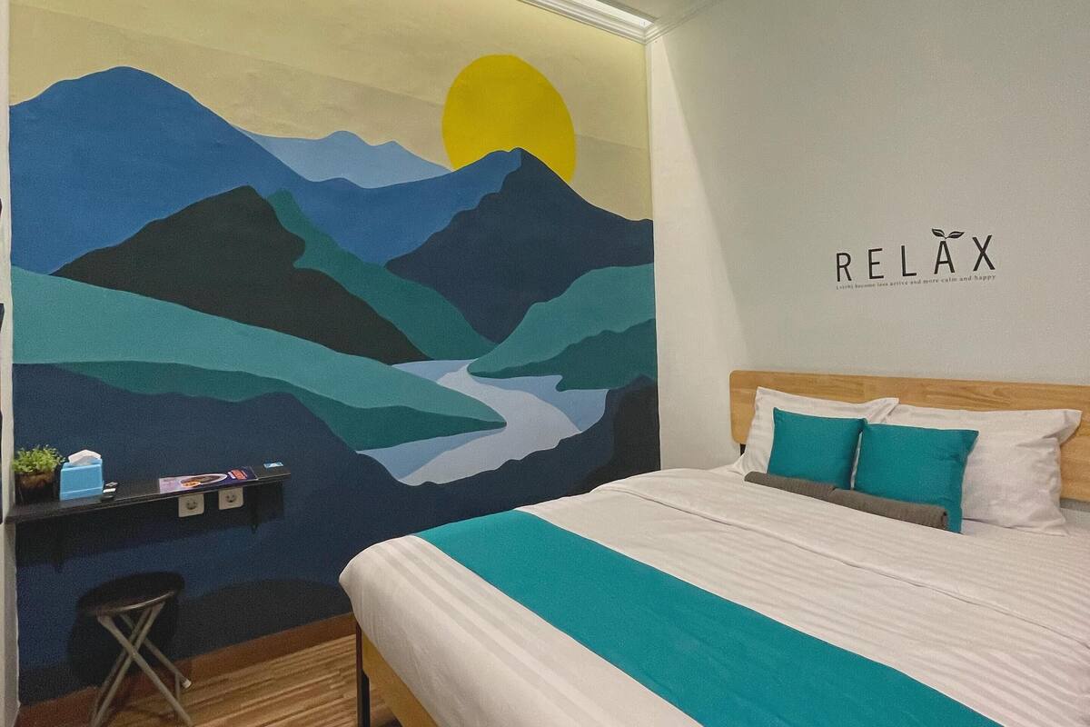 A bedroom with a bed, a desk with a chair, a wall mural, and a 'RELAX' sign.