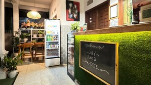 Un hostal acogedor con una pared verde, un cartel de pizarra, un refrigerador y un comedor con mesa y sillas.