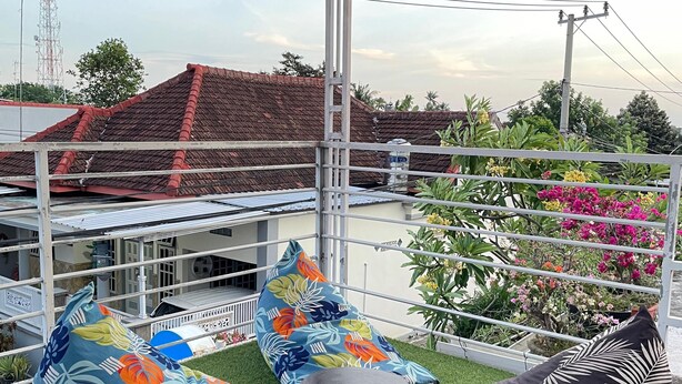 Una terraza en la azotea con asientos exteriores, vista a un edificio de tejado rojo y una torre de líneas eléctricas al fondo.