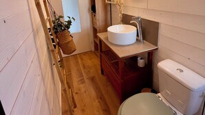 Een kleine badkamer met een houten vloer, een wit wastafelmeubel, toilet en een spiegel met verlichting.