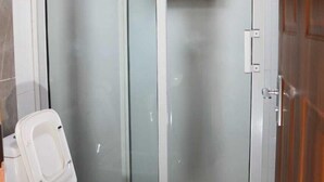 A bathroom with a toilet, a glass shower enclosure, and a wooden door. - old station lounge (Naivasha)