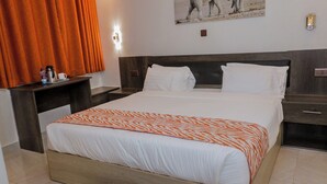 A hotel room with a bed, a nightstand, a wall-mounted light, and a painting. - old station lounge (Naivasha)