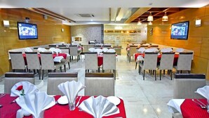 Un restaurante con varias mesas dispuestas para comer, cada una con mantel blanco y servilletas rojas.