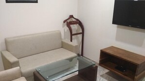 Una sala de estar con un sofá color crema, una mesa de centro de vidrio, un mueble de televisión de madera y un perchero de madera.