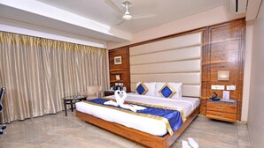 Una habitación de hotel con una cama grande, cabecera de madera, mesita de noche, escritorio y ventilador de techo.