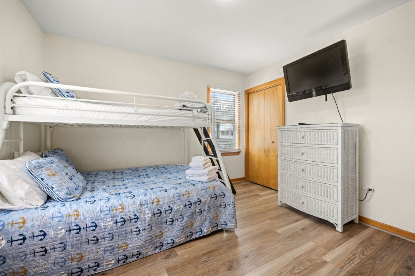 Ein Etagenbett mit gemustertem Bettbezug, eine weiße Kommode und ein an der Wand befestigter Fernseher.