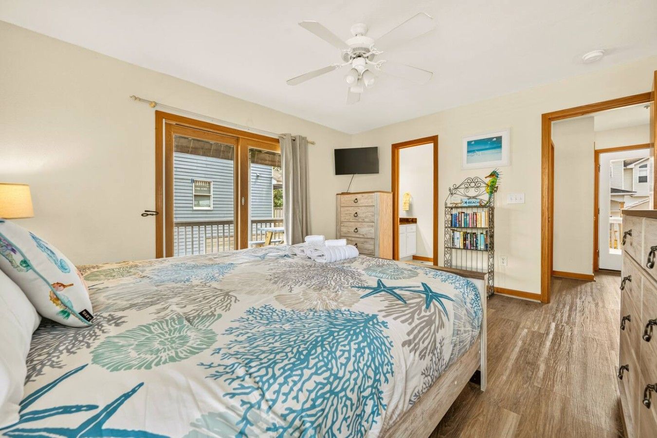 A bedroom with a bed, a ceiling fan, a TV, a bookshelf, and a view of the outside.