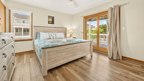 Une chambre avec un lit en bois, un ventilateur de plafond, une fenêtre avec des stores, une commode et une vue sur l’extérieur.