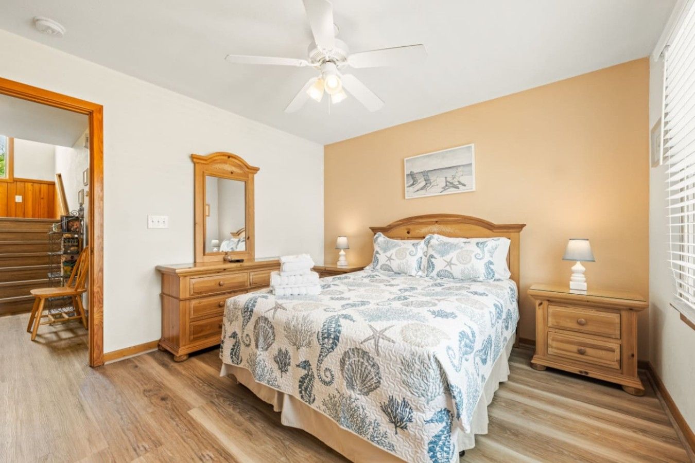 A bedroom with a bed, bedside tables, a mirror, a ceiling fan, and a window with blinds.