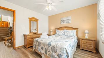 A bedroom with a bed, bedside tables, a mirror, a ceiling fan, and a window with blinds.