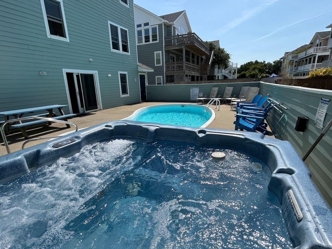 A hot tub with a pool, outdoor seating, and a building in the background.