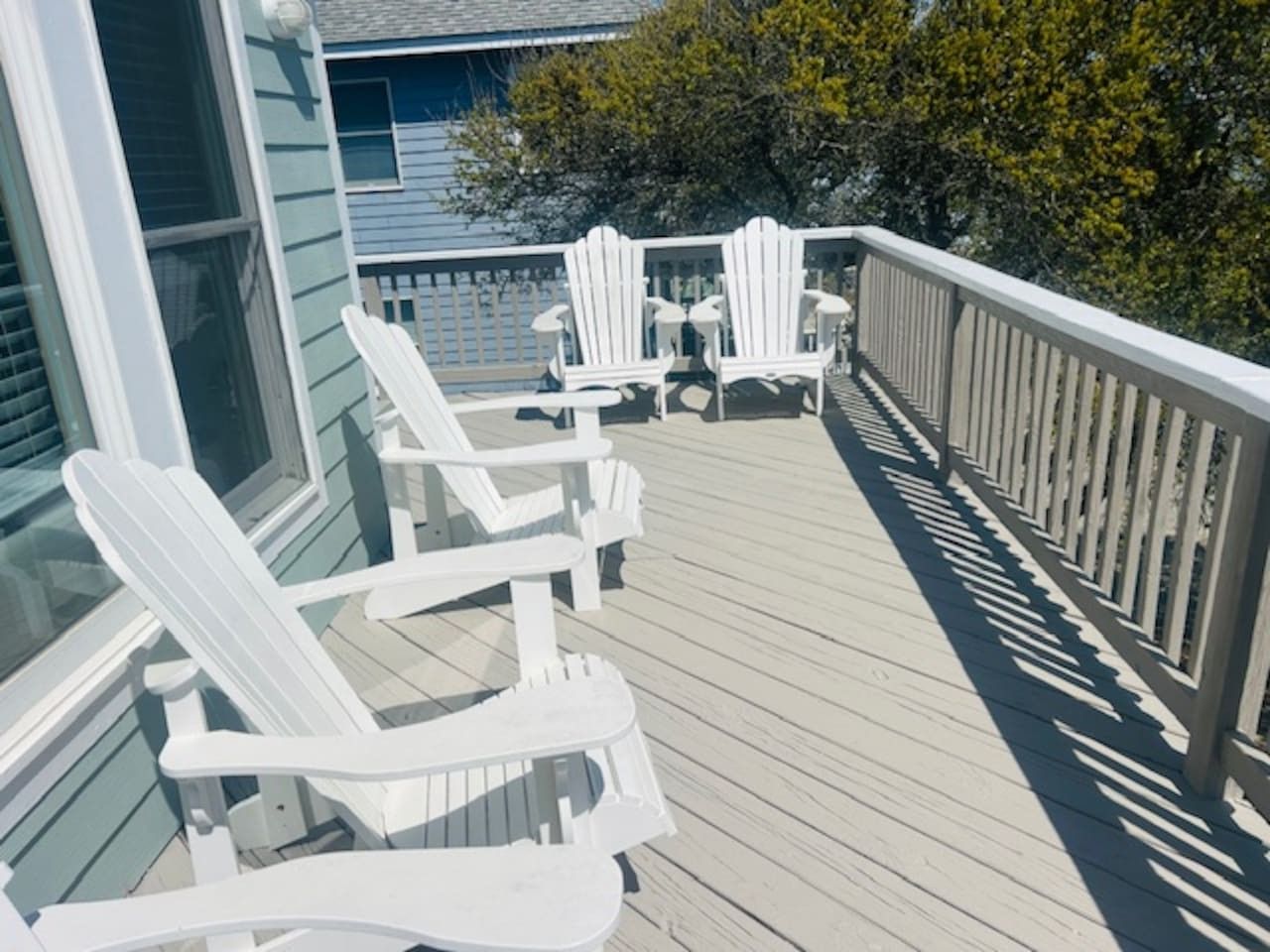 Eine Holzterrasse mit weißen Adirondack-Stühlen und einem Geländer.