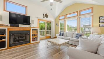 A spacious living room with a fireplace, a television, and a ceiling fan.