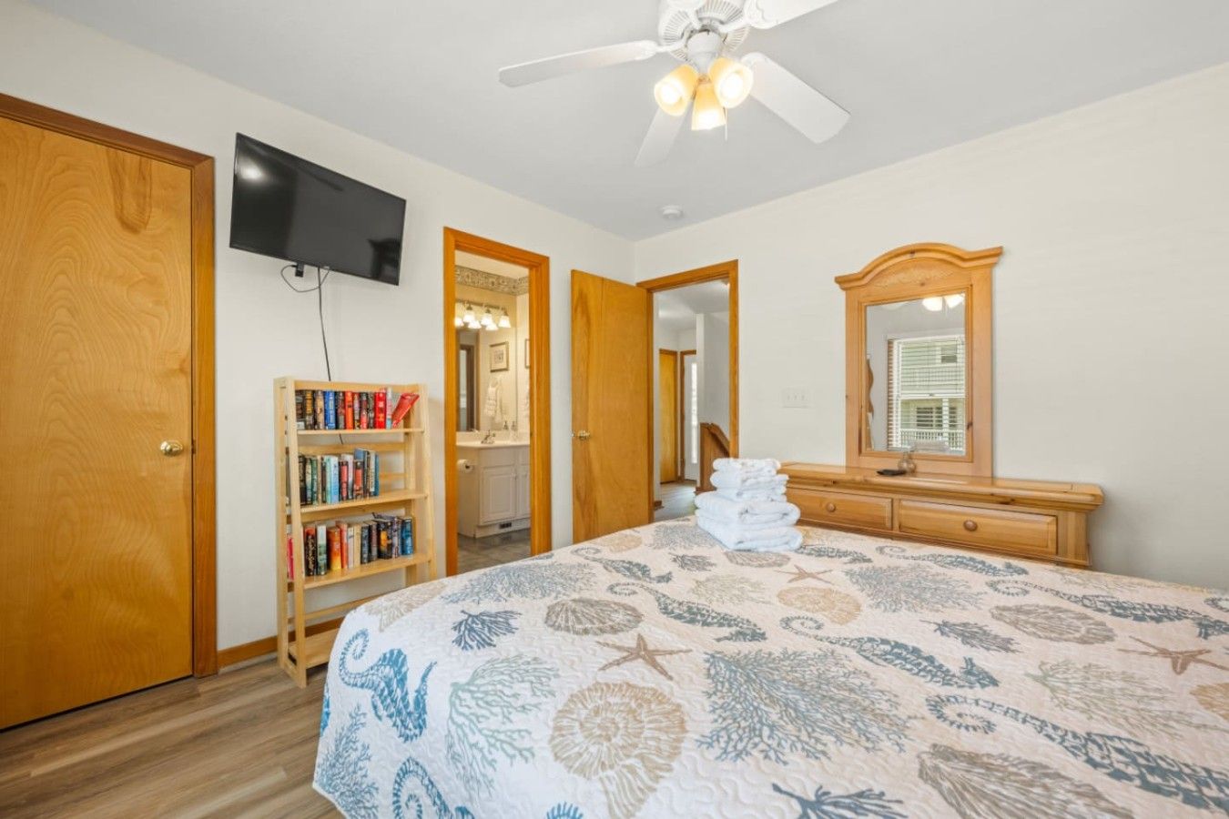 A bedroom with a bed, a bookshelf, a television, a ceiling fan, and a bathroom visible through an open door.