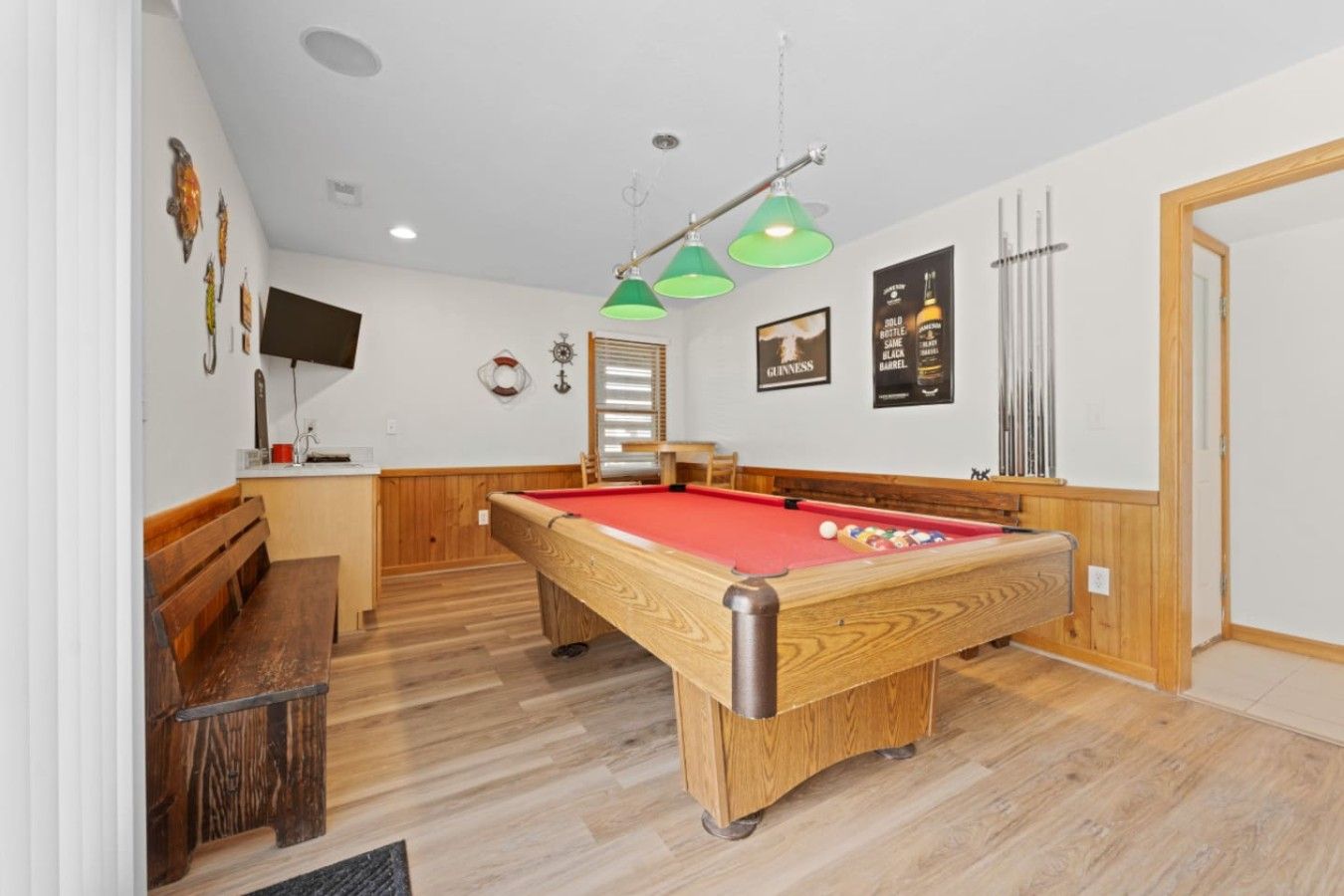 Een pooltafel in een ruimte met houten vloeren, een bank en een televisie aan de muur.