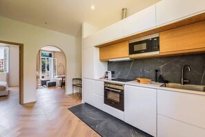 Een moderne keuken met witte kastjes, een zwart marmeren achterwand en een ingebouwde magnetron.