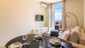 A dining area with a table set for four, a sofa, a TV, and a window with a view. - Elegant one-bedroom apartment with sea view at the gateway to Monaco (Beausoleil)