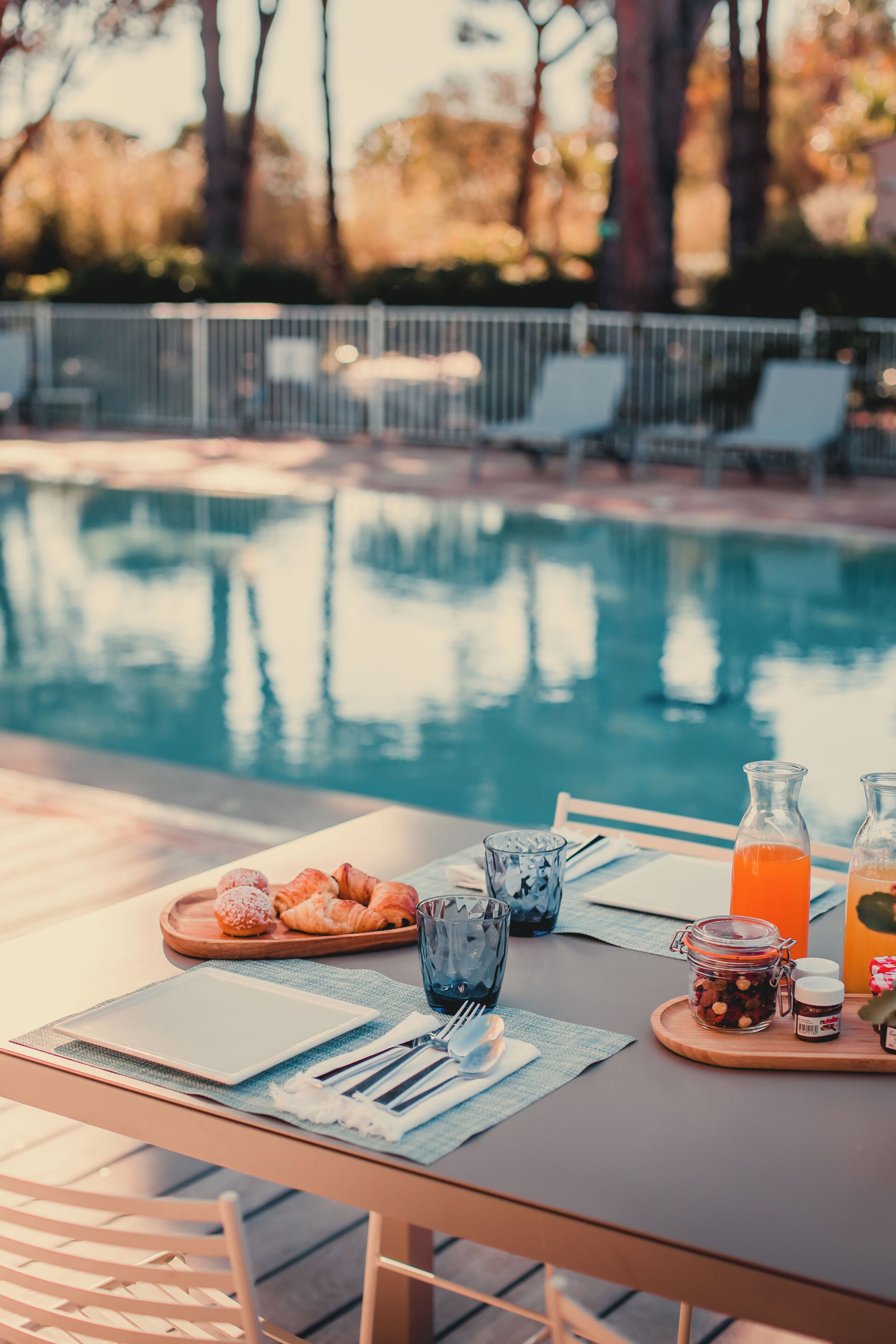 A poolside table with breakfast items, a glass of orange juice, and a bottle of water.