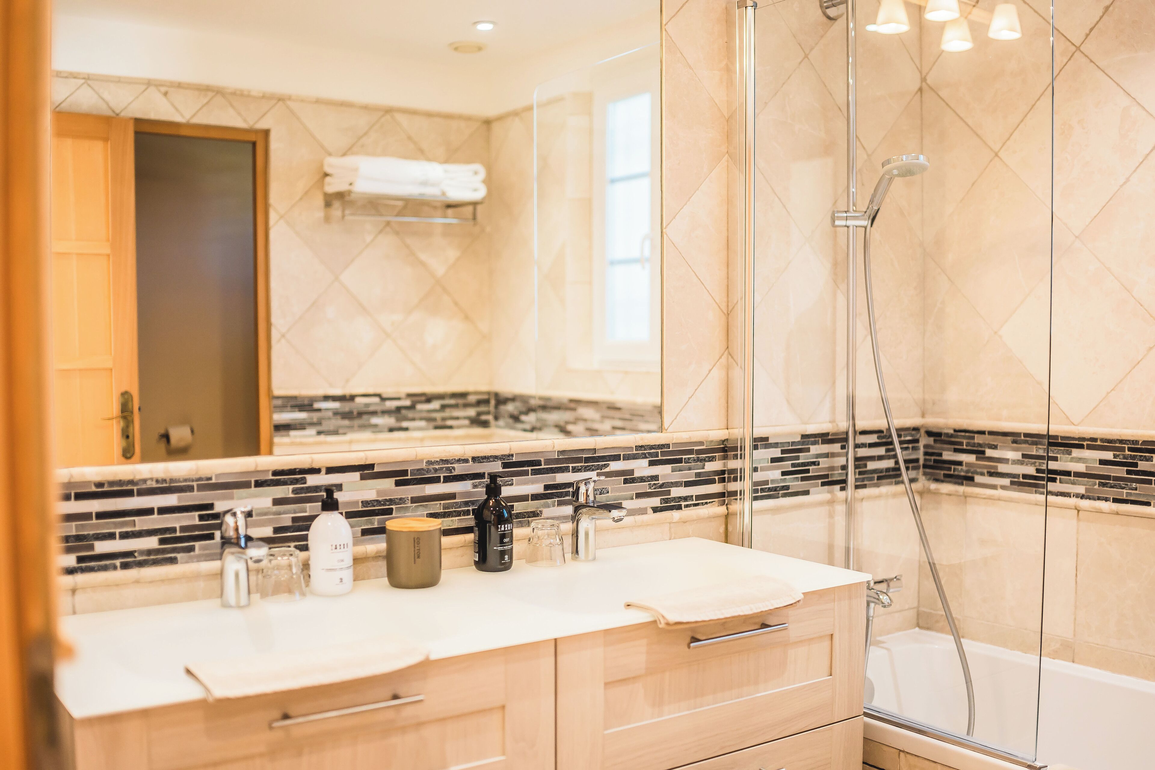 A modern bathroom with two sinks, a glass shower enclosure, and a tiled backsplash.