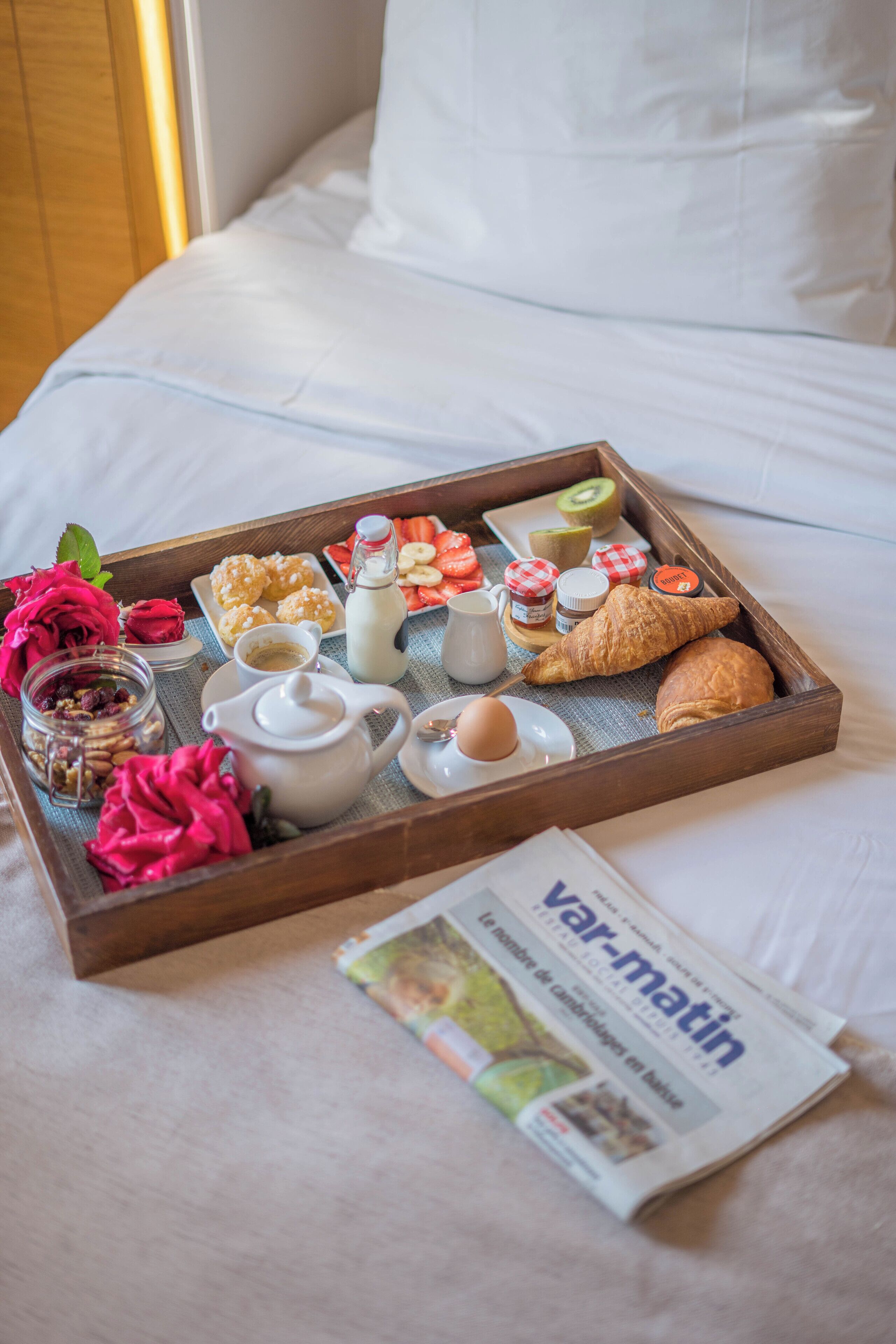Una bandeja de desayuno con pasteles, frutas y bebidas sobre la cama.