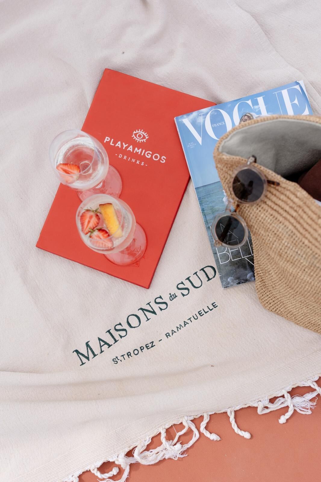 Un artículo de viaje con un librito rojo, una revista y un bolso de paja con gafas de sol.