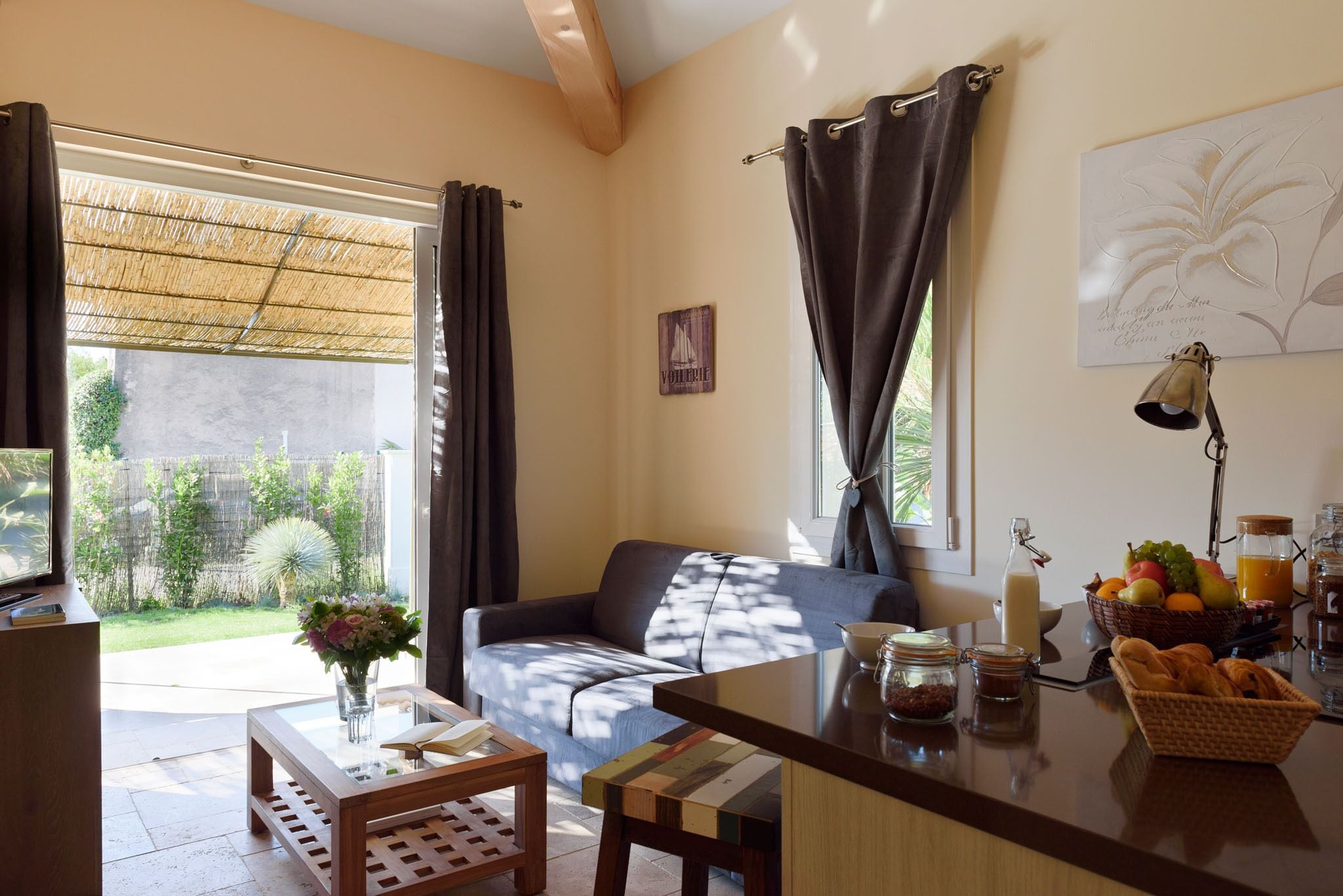A living room with a sofa, coffee table, and a dining area with a basket of bread and fruit.