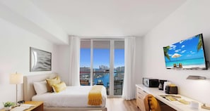 Habitación de hotel moderna con cama, escritorio, televisor y balcón con vistas a la ciudad.