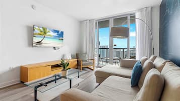 A modern living room with a large window, a flat-screen TV, a sofa, a glass coffee table, and a wooden cabinet.