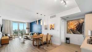 A modern living room with a dining area, large windows, and a city view. - Top Luxury Apartment with Pool & Gym (Hallandale Beach)