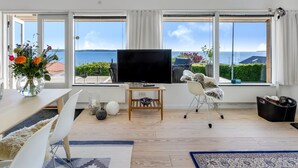 A modern living room with a large TV, white furniture, and a view of the sea. - "Tobias" - 45m to the fjord by Interhome (Børkop)