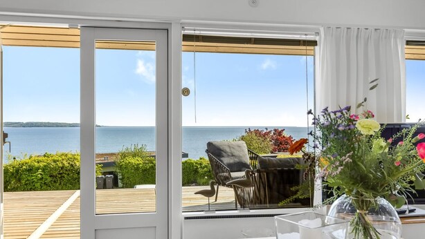 A room with a view of the sea, a dining area with a table and chairs, and a vase with flowers. - "Tobias" - 45m to the fjord by Interhome (Børkop)