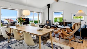 A modern living room with a wooden dining table, comfortable seating, a fireplace, and large windows offering a view of the sea. - "Tobias" - 45m to the fjord by Interhome (Børkop)