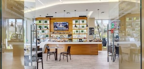 A bar area with a wooden counter, multiple shelves of bottles, a television screen, and a seating area with chairs. - Studio with Pool, gym and Amenities (Hallandale Beach)