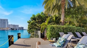 Un patio frente al agua con sillones, una mesita y vistas al puerto deportivo y edificios.