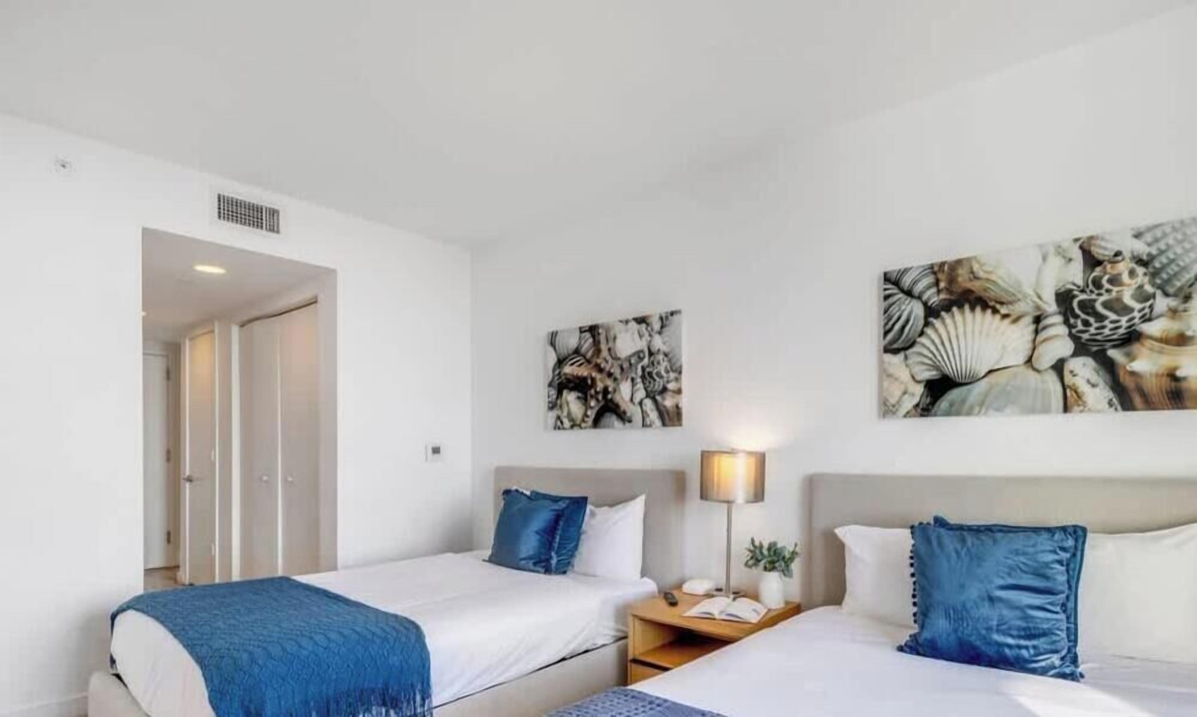 A hotel room with two beds, a nightstand, a lamp, and artwork on the walls.