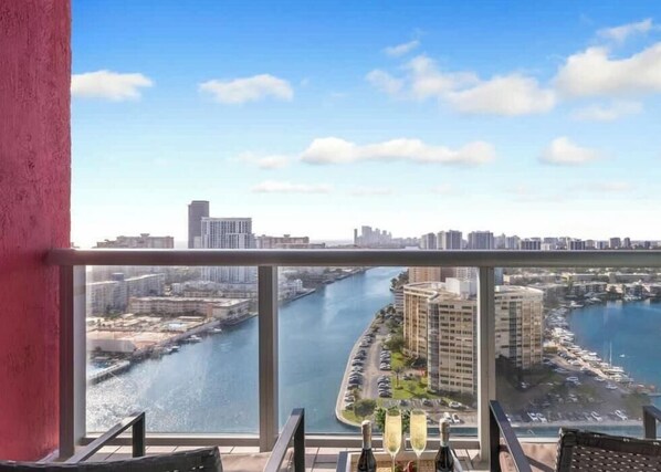 A balcony with a city view, a table with bottles, and a chair.