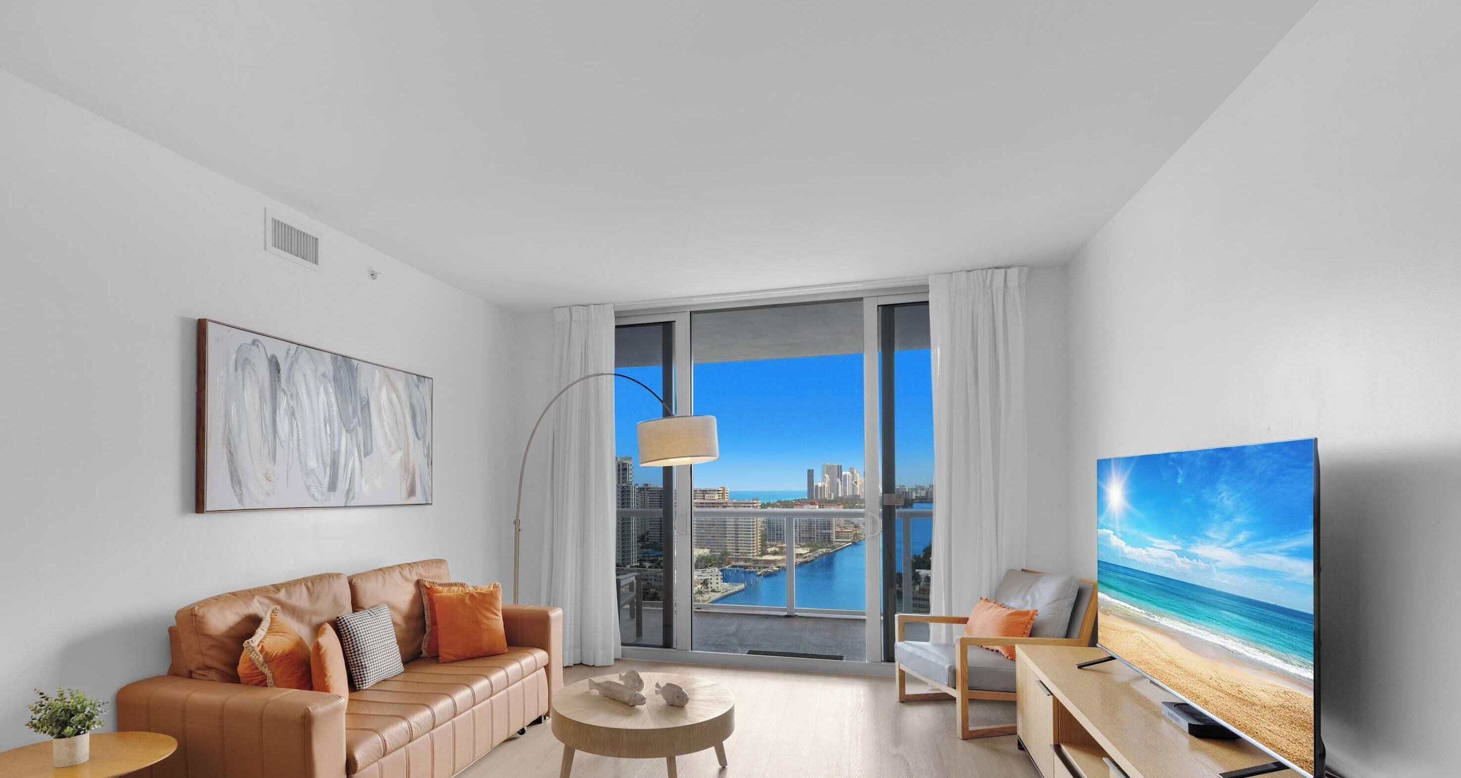 A modern living room with a sofa, coffee table, TV, and a large window with a city view.