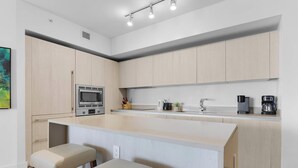 A modern kitchen with light wood cabinets, a built-in microwave, a coffee maker, and a sink. - Serenity by the Sea |  Balcony Views + Resort Pool (Hollywood)