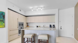 A modern kitchen with a central island, stainless steel appliances, and a minimalist design. - Serenity by the Sea |  Balcony Views + Resort Pool (Hollywood)