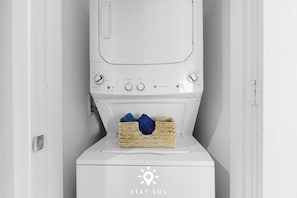 A white washing machine with a basket of blue towels on top. - Serenity by the Sea |  Balcony Views + Resort Pool (Hollywood)