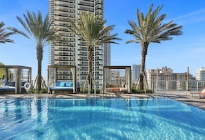 A rooftop pool with palm trees and a high-rise building in the background.