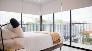 A modern bedroom with a large bed, a bedside table with a lamp, and a view of the city through large windows. - w* | Amazing 3BR w/ Balcony in Miraflores (Miraflores)