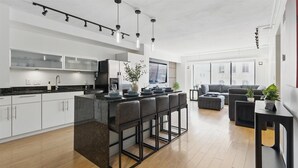 A modern kitchen with a central island, bar stools, and a dining area with a sofa and ottoman. - Modern Flat in the Heart of Indianapolis (Indianapolis)