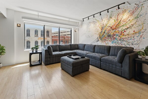 A modern living room with a sectional sofa, a small table, and a large abstract painting on the wall.