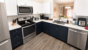 Una cocina moderna con armarios blancos, electrodomésticos de acero inoxidable, microondas, horno, tostadora y cafetera.