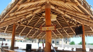 Un bar tiki con techo de paja, vigas de madera y un letrero.